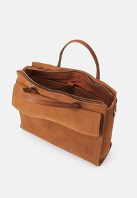 Tan suede käsilaukku, jolla on jämäkkä muoto, kaksi kahvaa, ulkopuolinen läppäpocket ja vetoketjullinen pääosasto. Sisäosa on vuorattu ruskealla kankaalla.