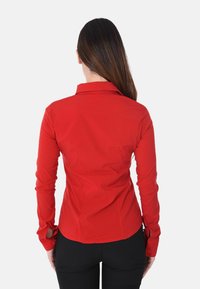 Camicia rossa a maniche lunghe con collo strutturato, design aderente e polsini abbottonati. Tessuto liscio e orlo dritto sul retro.