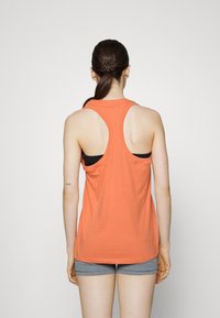 Top in arancione senza maniche con design racerback, realizzato in materiale morbido. Un reggiseno sportivo nero appare attraverso i ritagli posteriori. Sono visibili dei pantaloni corti grigi.