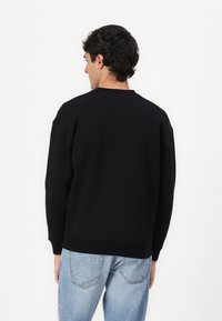 Schwarzer Sweatshirt mit Rundhalsausschnitt, gerippten Bündchen und Saum, im lässigen Schnitt. Getragen mit hellblauen Jeans.