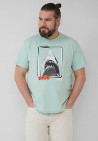 Mintgroene T-shirt met een graphic van een haai met een open mond, "JAWS" in het rood en "1975" in het wit, gemaakt van zachte katoen.