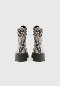 Schlangenleder-musterte Ankle Boots in Beige und Schwarz, mit einer strukturierten Oberseite, dicker schwarzer Gummisohle und Anziehhilfen für ein einfaches Anziehen.