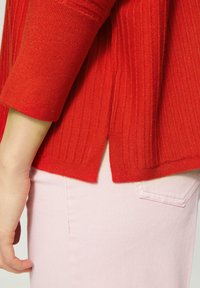 Rood geribbelde trui met 3/4 mouwen, voorzien van zijslashes. Gecombineerd met lichtroze denim broek met een achterzakdetail.