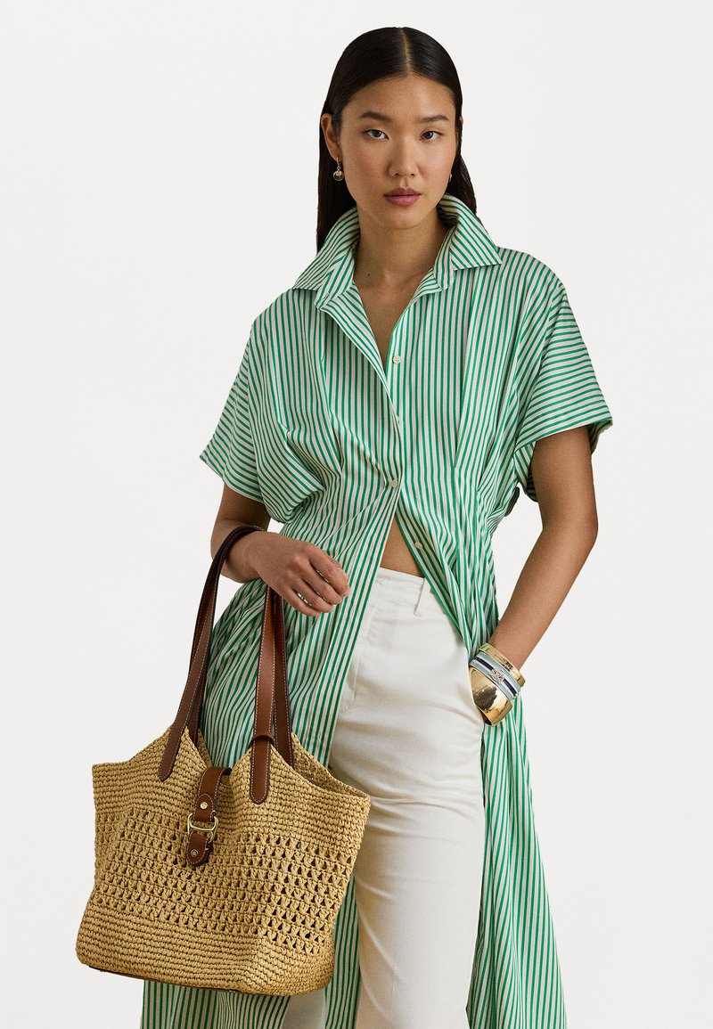 Πράσινη και λευκή ριγέ φαρδιά πουκάμισο με γιακά, συνδυασμένο με λευκά παντελόνια. Κρατώντας μια πλεκτή τσάντα από ψάθα με καφέ δερμάτινες λεπτομέρειες.