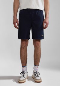 Navy shorts made of lightweight material, featuring an elastic waistband, side pockets, and a small logo patch on the left thigh.
