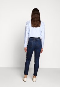 Chemise à manches longues bleu clair associée à un jean skinny bleu foncé. Coupe décontractée, matière coton, avec poches arrière et design minimaliste. Chaussures beige.