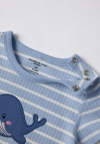 Vaaleansininen raidallinen potkupuku, jossa on valasapplikaatio, olkapäällä painonapit ja resorikuvio. Brändin etiketti näkyvissä sisäpuolella.