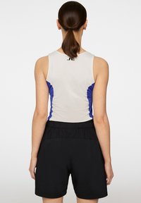 Top da allenamento senza maniche di colore grigio chiaro con pannelli laterali blu, abbinato a pantaloni corti neri con vita elastica. Tessuto liscio con leggero lucido.