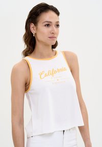 Valge lühike tops kollase ä�äre ja "California Bigstar since 1979" printimisega. Valmistatud pehmest puuvillakangast, sisaldab vabalt langevat lõiget.