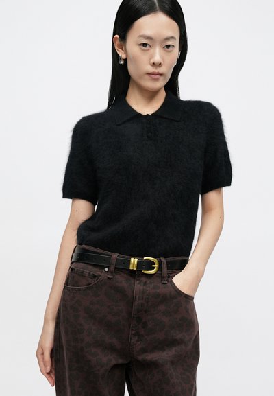 Čierny polokošeľový sveter s krátkym rukávom, mäkkou, chlpovou textúrou a zapínaním na tri gombíky, doplnený tmavohnedými džínami s leopardím vzorom a čiernym opaskom.