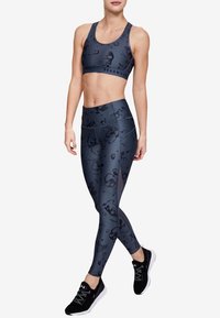 Top e leggings sportivi grigio scuro con un motivo astratto sottile. Il materiale sembra elastico. Indossati con scarpe da ginnastica nere.