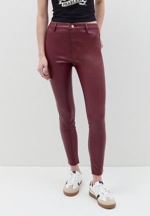 Burgunderrot faux Leder Skinny-Hosen mit glatter Textur, frontalen Taschen und Knopfverschluss; kombiniert mit weißen Sneakers.