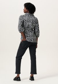 Zebraprint shirt in zwart-wit, relaxte pasvorm, driekwartmouwen, gecombineerd met donkere jeans en zwarte schoenen, bekeken van achteren.