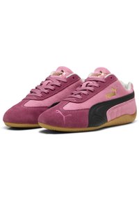 Ein Paar rosa Wildleder-Sneaker von Puma mit schwarzen seitlichen Streifen, gummifarbenen Sohlen und goldenen Puma-Logos auf der Zunge und den Seiten.