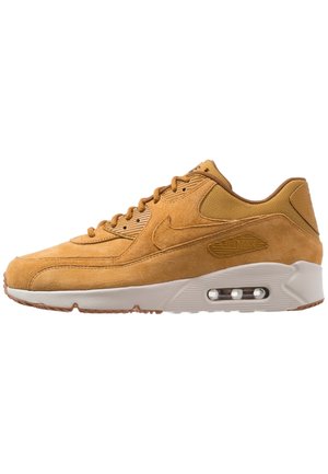 Baskets Nike Air Max en daim beige avec coussin d’air visible dans la semelle blanche, design à lacets et détails en tissu texturé au talon et à la languette.