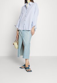 Camicia a righe azzurra, con bottoni, taglio largo; abbinata a una gonna di jeans al ginocchio con spacco frontale; sandali blu con dettagli in frange.