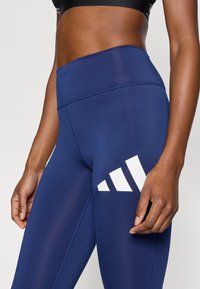 Μπλε σκούρο αθλητικό κολάν με ψηλό ζωνάρι μέσης, λεία υφή και μεγάλο λευκό γραφικό λογότυπο στο αριστερό μηρό.