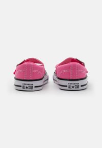 Zapatillas de lona rosas con diseño de caña baja, suelas de goma blanca y rayas negras. Cuenta con un lazo para facilitar su uso.