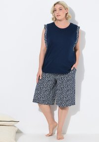 Marineblauwe mouwloze top met bloemenaccenten, gecombineerd met knielange shorts met een witte bloemenprint op een marineblauwe achtergrond.
