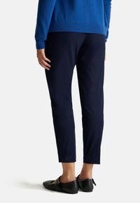 Granatowe, zwężane spodnie wykonane z gładkiego materiału, w połączeniu z czarnymi mokasynami z ozdobnymi akcentami. Sweter jest w jednolitym, jasnoniebieskim kolorze.