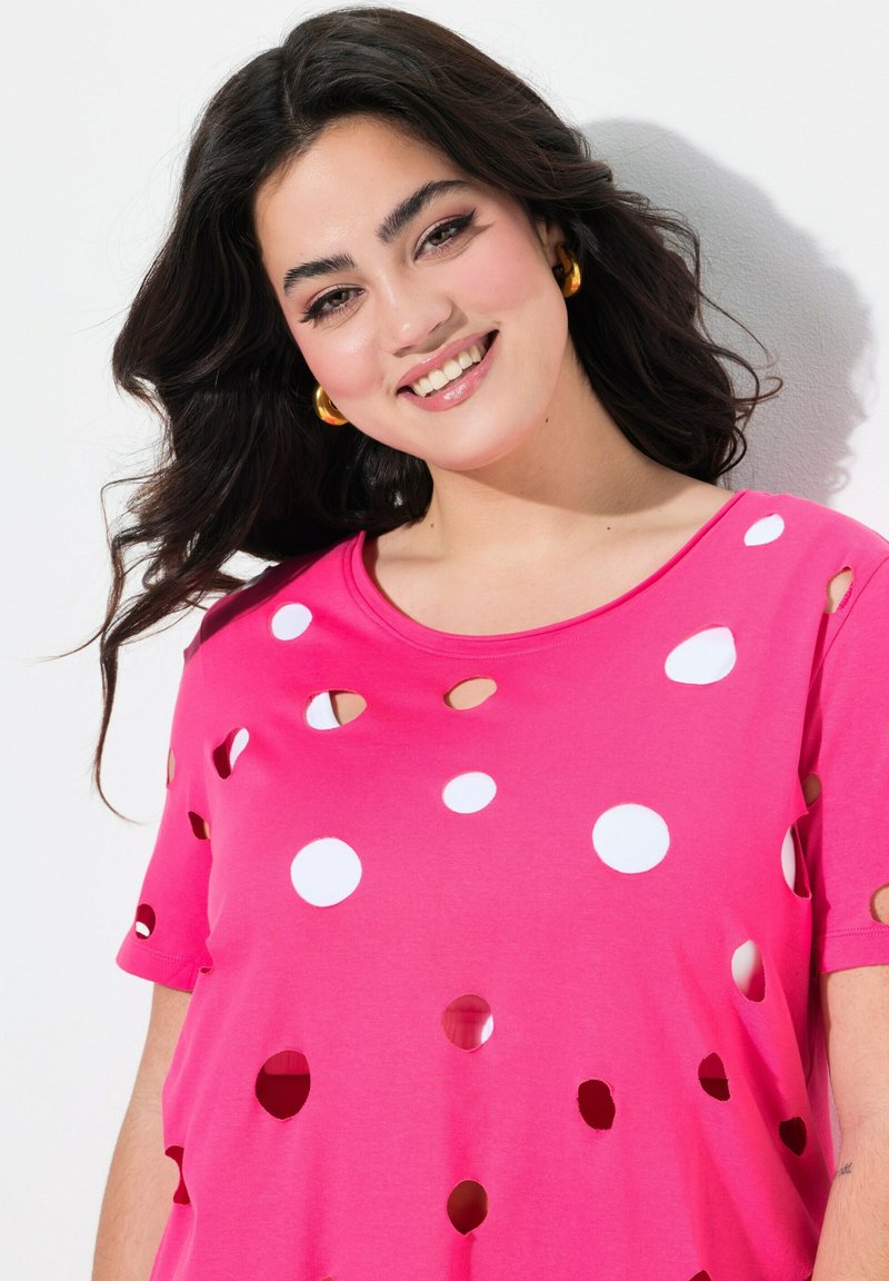 T-shirt rosa a maniche corte con vari fori circolari di diverse dimensioni, creando un motivo, realizzato in un tessuto morbido con una vestibilità rilassata.