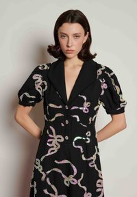 Μαύρο φόρεμα με βαθύ V-λαιμόκοψη, κοντά φουσκωτά μανίκια και μεταλλικές διακοσμήσεις σε κυκλωτά σχέδια. Διαθέτει διακοσμητικά κουμπιά και υφάσμα με υφή.