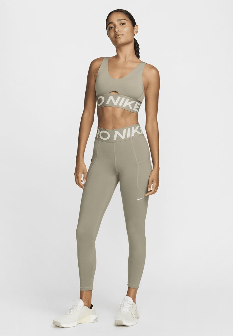 Conjunto de sujetador deportivo y mallas en verde oliva claro, con un detalle cortado, banda de logo en negrita y textura de tela suave y elástica.