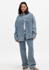 Jeansjacke und passende weit geschnittene Hose in Hellblau, mit strukturiertem Stoff, oversized Passform und großen Knöpfen.