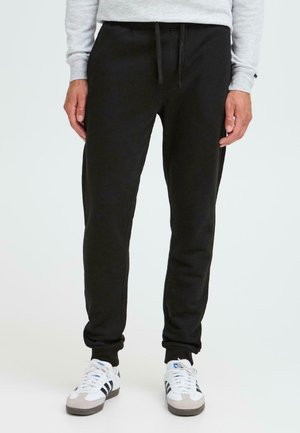 Sorte sweatpants lavet af blødt stof, med elastisk talje med snøre og tapered ben. Båret med hvide sneakers.