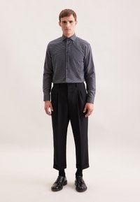 Pantaloni neri con orlo a risvolto, abbinati a una camicia a quadri scura con bottoni e scarpe in pelle nere. Tessuto morbido al tatto.