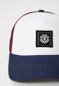 Casquette de baseball blanche avec des côtés en maille bordeaux et un visière marine. Présente un patch carré noir avec un logo d'arbre blanc à l'avant.