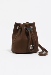 Bolso marrón de ante con cordón, ojales plateados, un detalle negro y un logo de marca en el frente; cuenta con una única correa para el hombro.