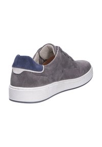 Zapatilla casual de ante gris con suela gruesa blanca y lengüeta trasera de ante azul, vista desde la parte trasera lateral sobre fondo blanco.