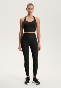 Čierna športová podprsenka s širokým výstrihom a dizajnom do V, skombinovaná s čiernymi legínami s vysokým pásom, ktoré majú diagonálne švy.