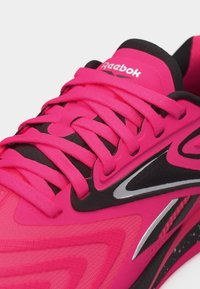 Κοντινή λήψη φωτεινού ροζ αθλητικού παπουτσιού Reebok με μαύρες και ασημένιες λεπτομέρειες και κορδόνια σε ταιριαστό ροζ χρώμα.