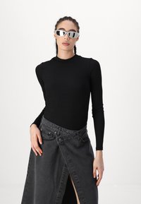 Black long-sleeve fitted top paired with a dark denim wrap skirt featuring a slit. Model wears silver reflective sunglasses.