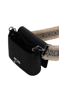 Sort rektangulær taske med en glat overflade, sølv hardware og en justerbar vævet rem med et geometrisk mønster i beige og sort.