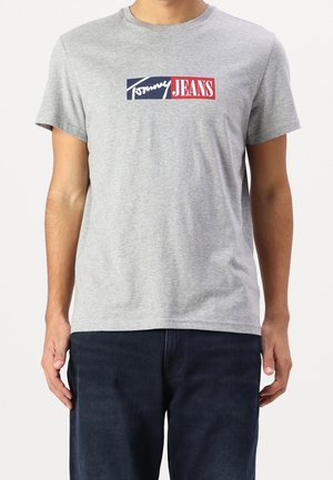 Gray cotton t-shirt featuring a rectangular logo with "Tommy" in white and "JEANS" in red, set against a navy background. Short sleeves, crew neck.