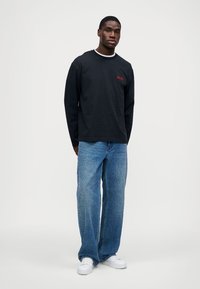 Fekete hosszú ujjú ing fehér gallérral, piros logóval; világoskék laza fazonú farmerrel és fehér sneakerrel párosítva. Egyszerű dizájn, hétköznapi stílus.