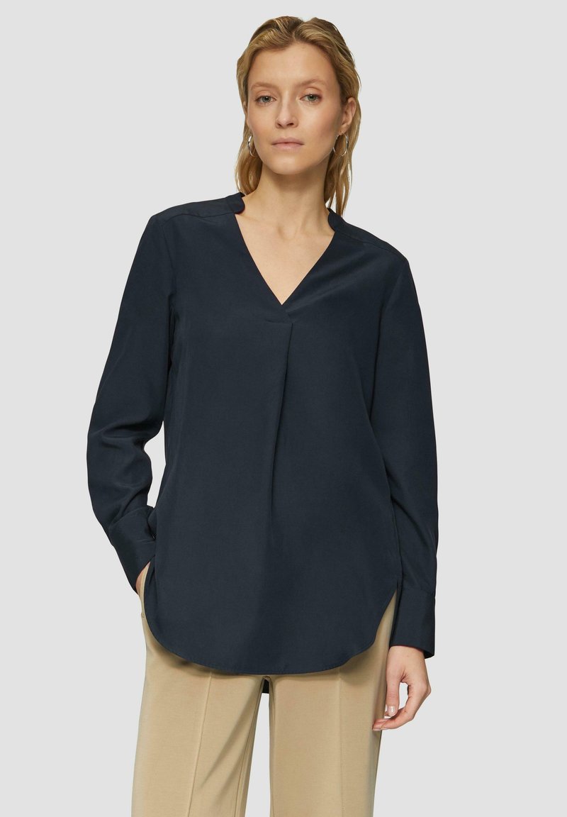 Blusa de manga larga azul marino con escote en V, aberturas laterales y una textura suave. Presenta un ajuste relajado y un minimalismo en los detalles.
