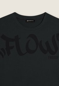 Camiseta de algodón negra con un gran gráfico tonal de "Flow". Diseño de cuello redondo con mangas cortas y una textura suave y lisa. Logo de Freddy en el lateral.