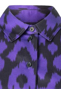 Violetti ja musta kuvioitu paita, jossa on kauluskangas, mustat napit ja sileä pinta. Suunnittelussa on abstrakti, piikikäs kuvio.