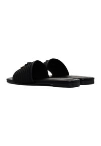 Sandali piatti neri con una parte superiore texturizzata, design open toe e una suola sintetica liscia. Accentuati da un elemento decorativo sulla cinghia.