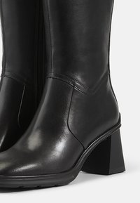 Black leather ankle boots with a square heel. Features a smooth texture, a side zipper, and curved seams.