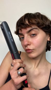 Piastra per capelli Revlon con finitura nera opaca e dettagli rossi, tenuta in mano. Presenta un design elegante con una piastra piatta in ceramica.