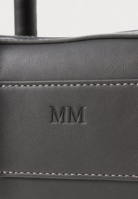 Svart skinnveske med teksturert finish, med hevet "MM"-logo og kontrasterende hvite sømmer langs sømmene.