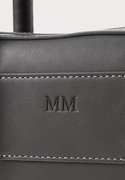 Črna usnjena torba z teksturirano površino, ki ima vtisnjen logo "MM" in kontrastno belo šivanje ob šivih.