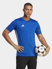 Kék rövid ujjú sportpóló, fehér Adidas logóval és három csíkkal. Fekete nadrág. Fekete-fehér focilabdát tart.