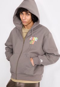 Gray zip-up hoodie made of cotton blend, featuring front pockets, drawstring hood, and colorful graphic on the left chest.