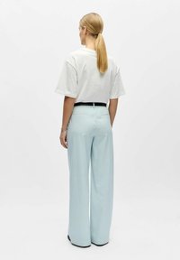 Valge lühikeste varrukatega t-särk, millel on helesinised triibulised laiade säärega püksid, millel must vöökoht ja taskud.